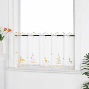 Die transparente Kurzgardine hängt festlich vor einem weißen Fenster. Die Gardine ist mit goldenen Nähten verziert und zeigt handgestickte Motive von Schneeflocken, Rentieren und einem Weihnachtsbaum, die eine weihnachtliche Atmosphäre schaffen. Die weiße Wand im Hintergrund sorgt für eine helle und neutrale Kulisse, während die pflanzlichen Dekorationen rund um das Fenster eine natürliche und gemütliche Stimmung verleihen. Der transparente Stoff lässt viel Tageslicht herein und sorgt für eine subtile, aber