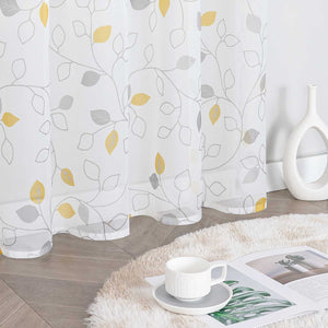 Dieser weiße Voile-Vorhang mit grauen Zweigen und gelb-grauen Blättern ist leicht und durchscheinend. Neben dem Vorhang steht eine weiße Vase, auf dem flauschigen Teppich liegen eine Tasse mit Untertasse und ein Magazin. Der Vorhang eignet sich perfekt für die Heimdekoration und schafft eine warme, helle Atmosphäre mit natürlichem Flair. Er wird häufig im Wohnzimmer oder Schlafzimmer verwendet.