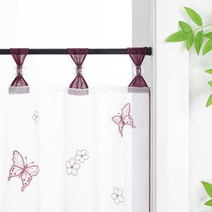 Nahaufnahme der lila Vorhangringe mit transparenten Perlen, der Vorhang hängt an einer Stange und zeigt Schmetterlingsmuster, daneben sind Blumen als Dekoration.
