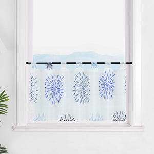 Die transparente Scheibengardine mit blauen Feuerwerksmotiven hängt vor einem Fenster. Der weiße Hintergrund lässt die blauen Muster des Feuerwerks strahlen und sorgt für eine festliche, aber beruhigende Atmosphäre im Raum.
