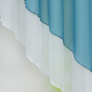 Nahaufnahme eines blauen halbtransparenten Gardinenstoffs mit gewellten, sanft fallenden Kanten. Das Licht hebt die feine Struktur des Stoffes hervor, während der Hintergrund in einem sanften Grünton verschwimmt.