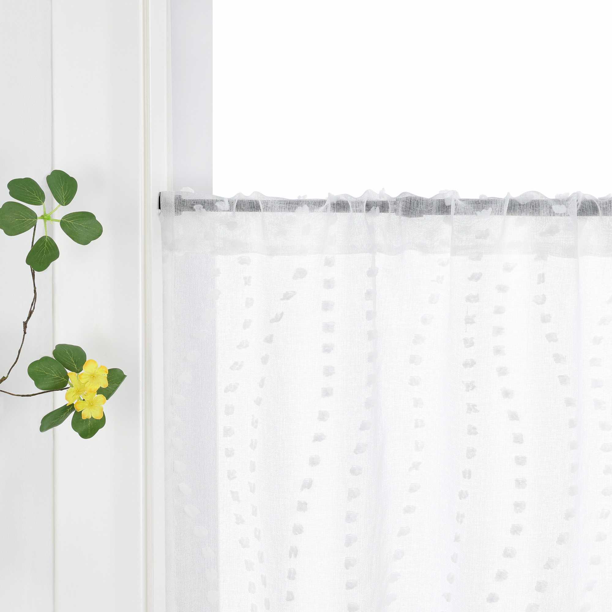 Die weiße Gardine mit dem 3D-Punktemuster hängt an einem Fenster, wobei die Aufhängung über die Schlaufen am Vorhangstab sichtbar ist. Das punktuelle Design der Gardine kommt klar zur Geltung und fügt dem Raum eine elegante Textur hinzu. Grüne Pflanzen am Fenster ergänzen das harmonische Gesamtbild und bringen Frische ins Zimmer.