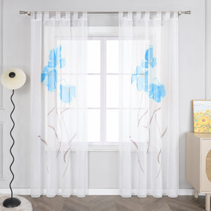 Das Bild zeigt einen Vorhang aus dünnem, weißen Stoff mit blauen Blumenmustern. Der Vorhang hat Riegel an der Oberseite, um ihn an einer Gardinenstange aufzuhängen. Neben dem Vorhang steht eine einzigartige Stehlampe, und auf dem kleinen Schrank rechts hängt ein Gemälde in Gelbtönen. 
