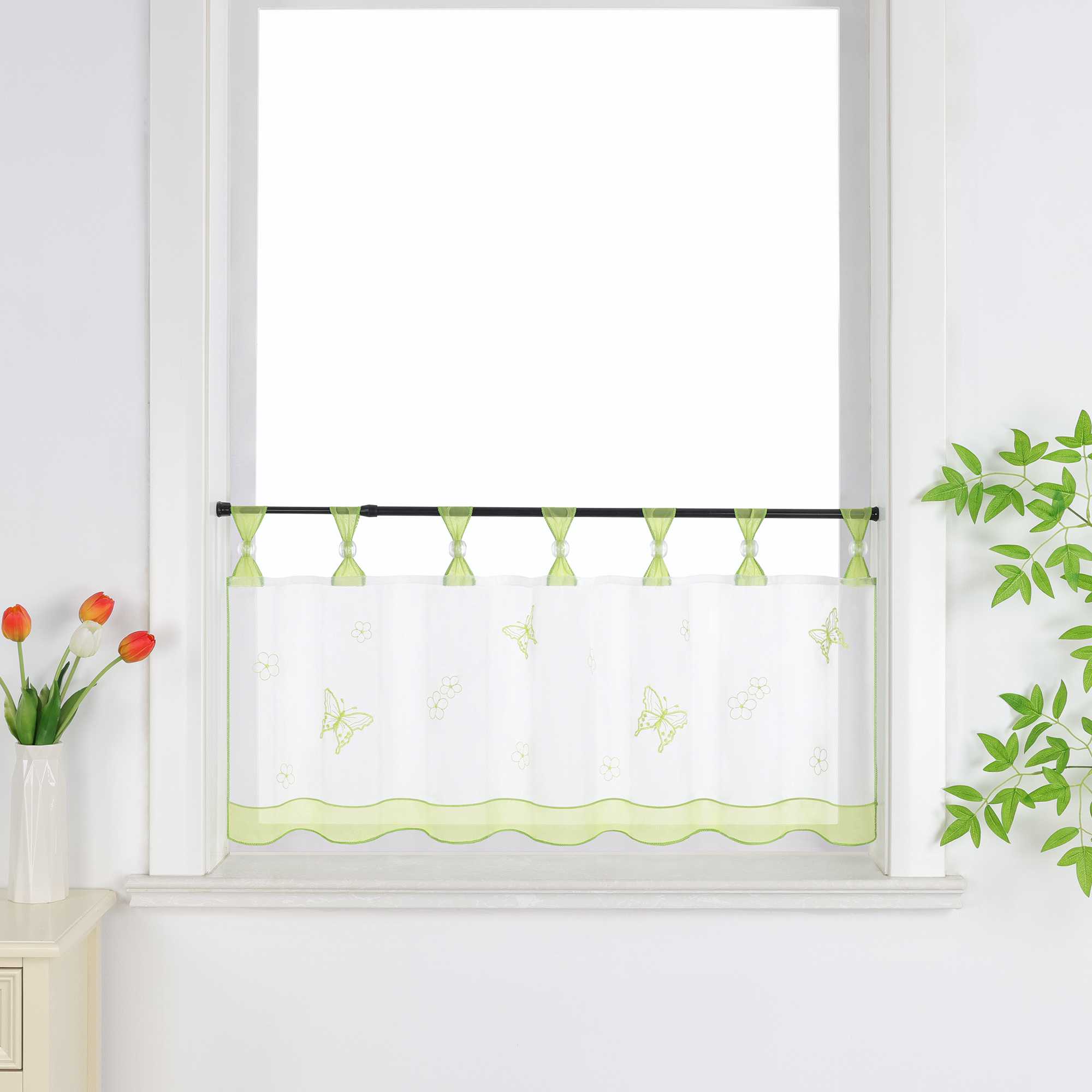 Gruen transparenter Schlaufen-Kurzvorhang mit dekorativen Perlen und Schmetterlingsmuster, verziert mit einem gruenen Dekoband am unteren Rand, aufgehängt neben einem Fenster mit Blumen und einem Schrank.