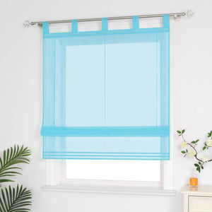 Halbtransparenter blauer Raffrollo hängt vor dem Fenster und sorgt für eine helle, luftige Atmosphäre. Daneben setzen grüne Pflanzen dekorative Akzente. Seitliche Ansicht.