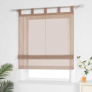 Halbtransparenter brauner Raffrollo hängt vor dem Fenster und sorgt für eine helle, luftige Atmosphäre. Daneben setzen grüne Pflanzen dekorative Akzente. Seitliche Ansicht.