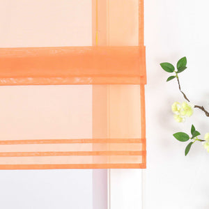 Detailansicht des unteren Bereichs eines halbtransparenten orangen Raffrollos. Der Stoff ist sanft hochgezogen und bildet dekorative Falten. Eine stilvolle Blumen-Deko neben dem Fenster rundet das Gesamtbild harmonisch ab.