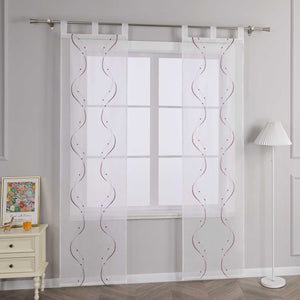 Joyswahl – Das Bild zeigt die Seitenansicht einer weissen transparenten Gardine mit Schlaufen, die an einer Metallstange haengt. Die Gardine ist mit lila Wellenperlenmuster und Stickerei versehen. Links vom Fenster steht ein heller Schrank mit Schubladen, auf dem ein farbenfrohes Blumenbild und ein orangefarbenes Objekt platziert sind. Rechts daneben steht eine Stehlampe mit weiss gestreiftem Lampenschirm.