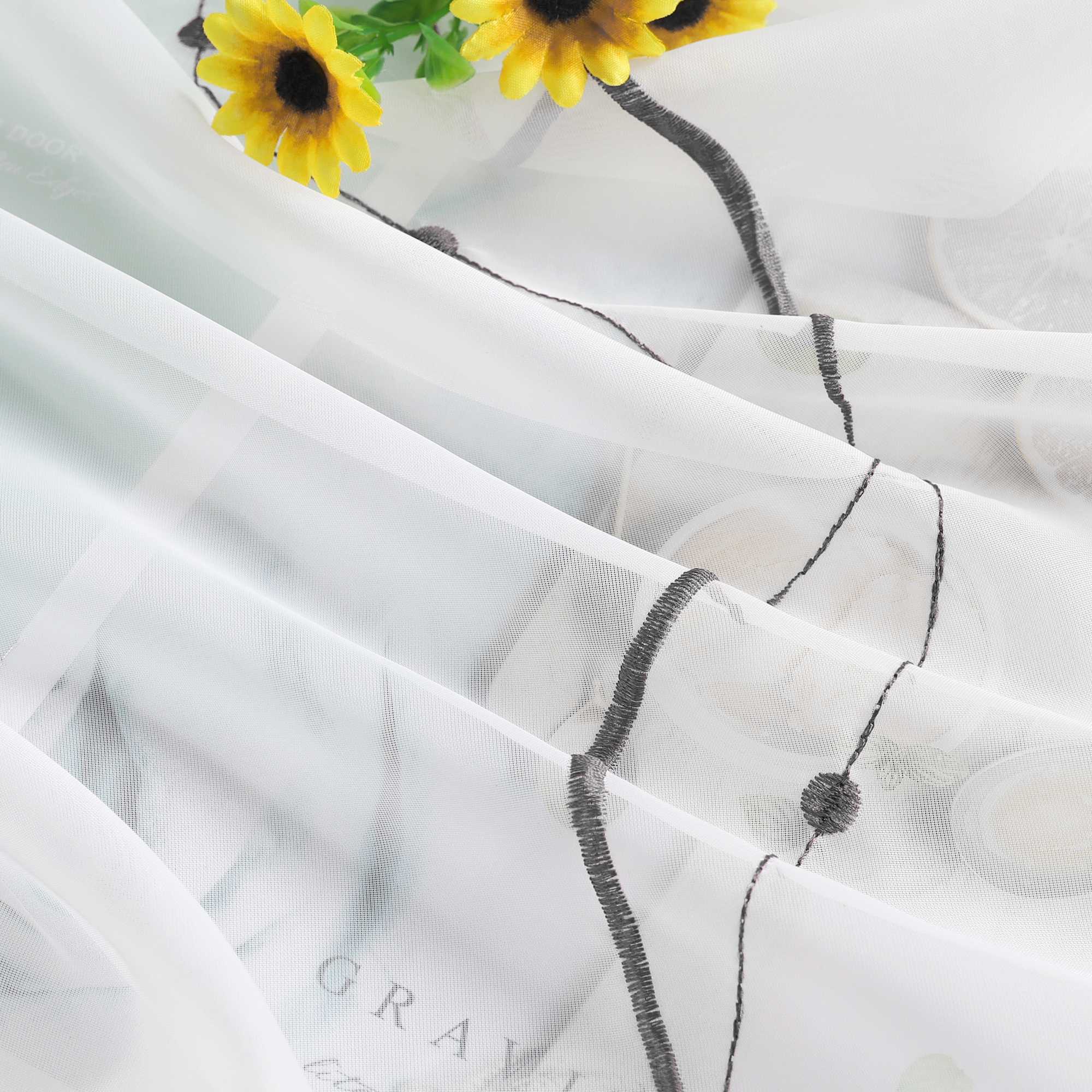 Ein weisser Stoff mit grauen Linienstrukturen und natuerlichen Falten. In der linken oberen Ecke befindet sich eine Sonnenblume.