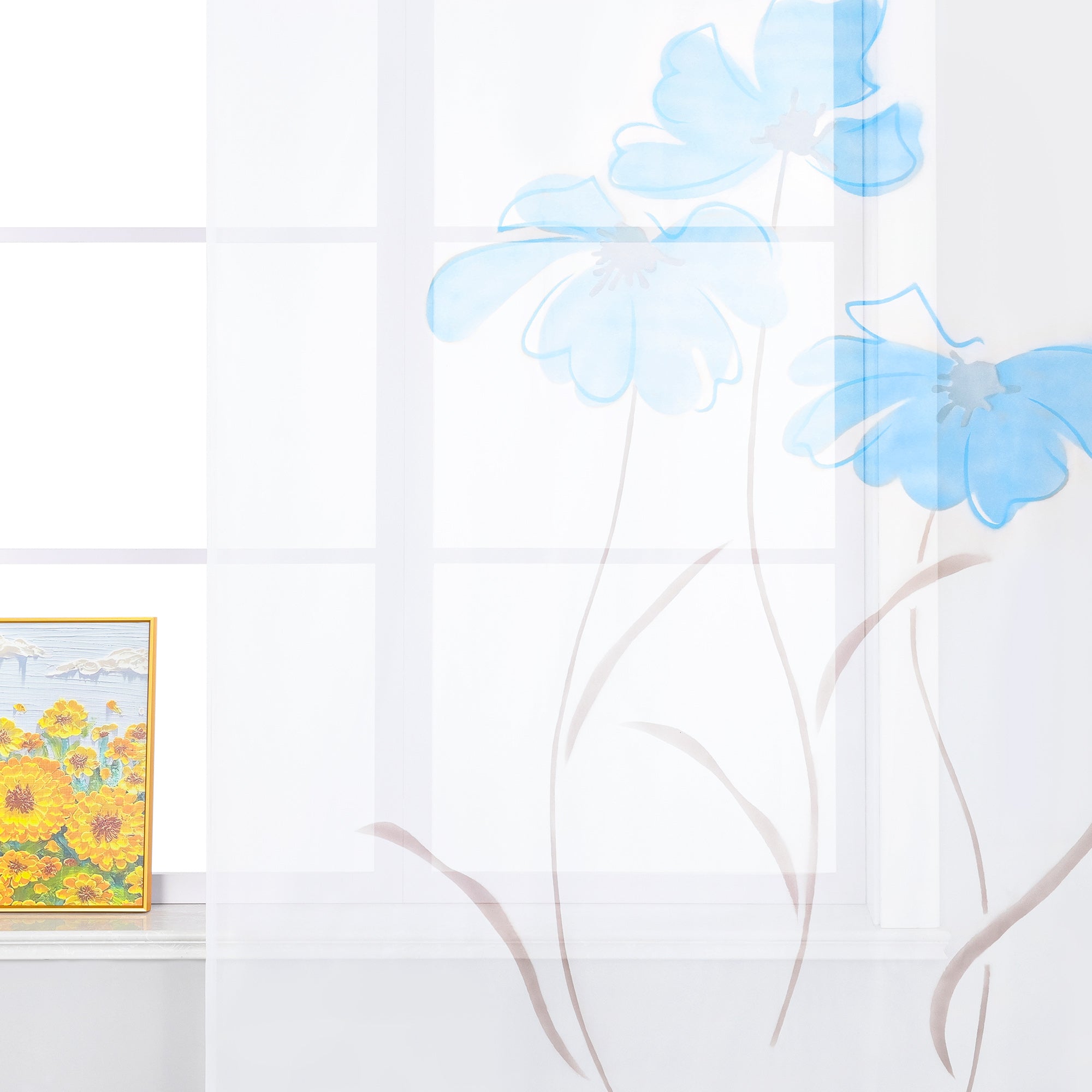 Das Bild zeigt einen weißen Vorhang mit blauen Blumenmustern. Das Design lässt die Blumen wie in der Luft schwebend erscheinen. Auf der Fensterbank steht ein dekoratives Bild, das gelbe Blumen darstellt. Insgesamt vermittelt die Szene einen frischen und hellen Eindruck.