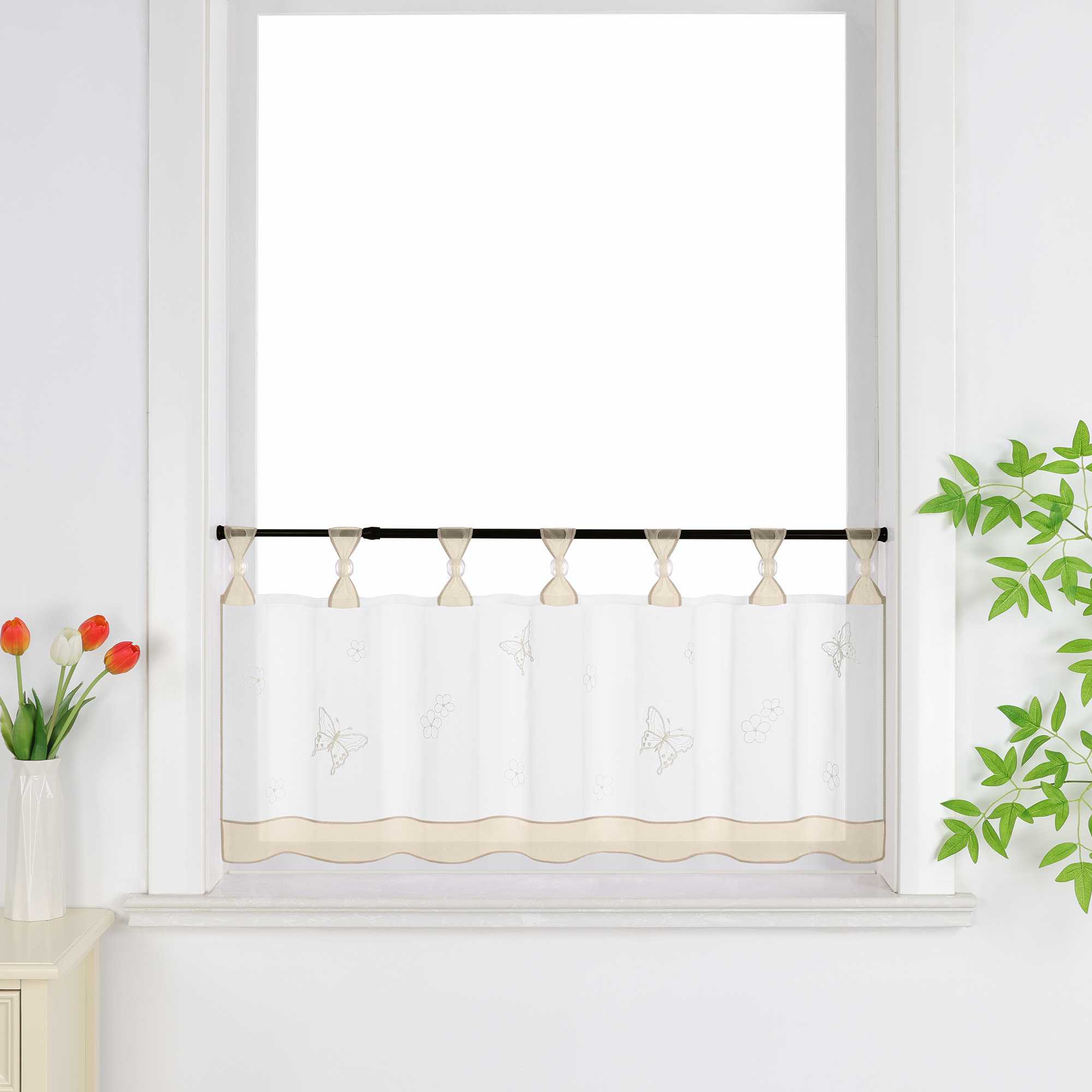 beige transparenter Kurzvorhang mit dekorativen Perlen und Schmetterlingsmuster, verziert mit einem beige Dekoband am unteren Rand, aufgehängt neben einem Fenster mit Blumen und einem Schrank.