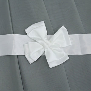 Dies ist ein Detailbild des Vorhangs. Auf dem grauen Stoff befindet sich ein weißes Webband, an dem eine weiße Schleife befestigt ist. Die Schleife ist fein gearbeitet und verleiht dem Vorhang eine elegante und dekorative Note.