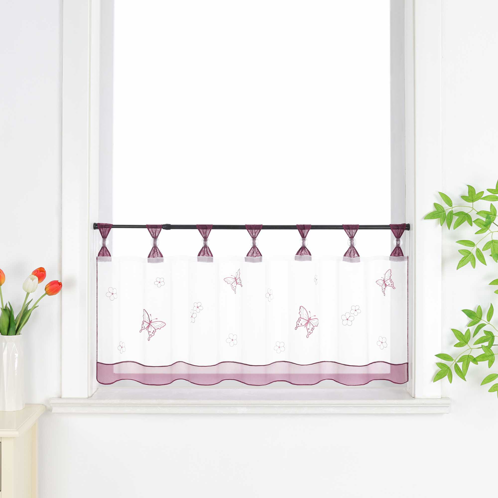lila transparenter Schlaufen-Kurzvorhang mit dekorativen Perlen und Schmetterlingsmuster, verziert mit einem lila Dekoband am unteren Rand, aufgehängt neben einem Fenster mit Blumen und einem Schrank.
