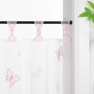 Nahaufnahme der rosa Vorhangringe mit transparenten Perlen, der Vorhang hängt an einer Stange und zeigt Schmetterlingsmuster, daneben sind Blumen als Dekoration.