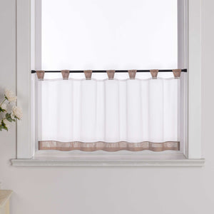Die braune Scheibengardine hängt vor einem Fenster, wobei die Hintergrundwand weiß ist. Der Vorhang ist transparent und wird von blumigen Dekorationen an der Seite begleitet.