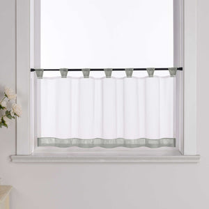 Die graue Scheibengardine hängt vor einem Fenster, wobei die Hintergrundwand weiß ist. Der Vorhang ist transparent und wird von blumigen Dekorationen an der Seite begleitet.