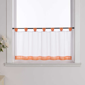 Die orange Scheibengardine hängt vor einem Fenster, wobei die Hintergrundwand weiß ist. Der Vorhang ist transparent und wird von blumigen Dekorationen an der Seite begleitet.