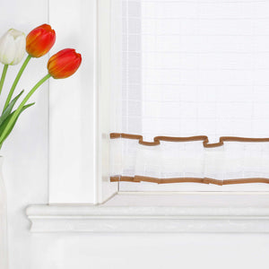 Nahaufnahme der unteren Fensterhälfte mit weißem, transparentem Kurzvorhang. Der untere Rand ist mit einer gewellten, braunen Borte verziert. Links im Bild stehen rote, orangefarbene und weiße Tulpen in einer Vase.